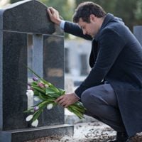 grieving man places flowers at grave