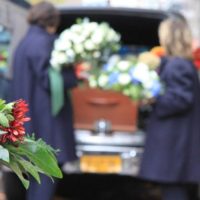 pallbearers load casket into hearse flanked by flowers